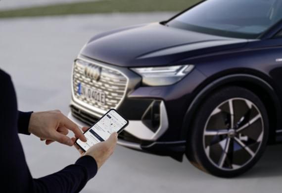 In the background is a Q4 e-tron.
In the foreground, someone is checking the myAudi app.